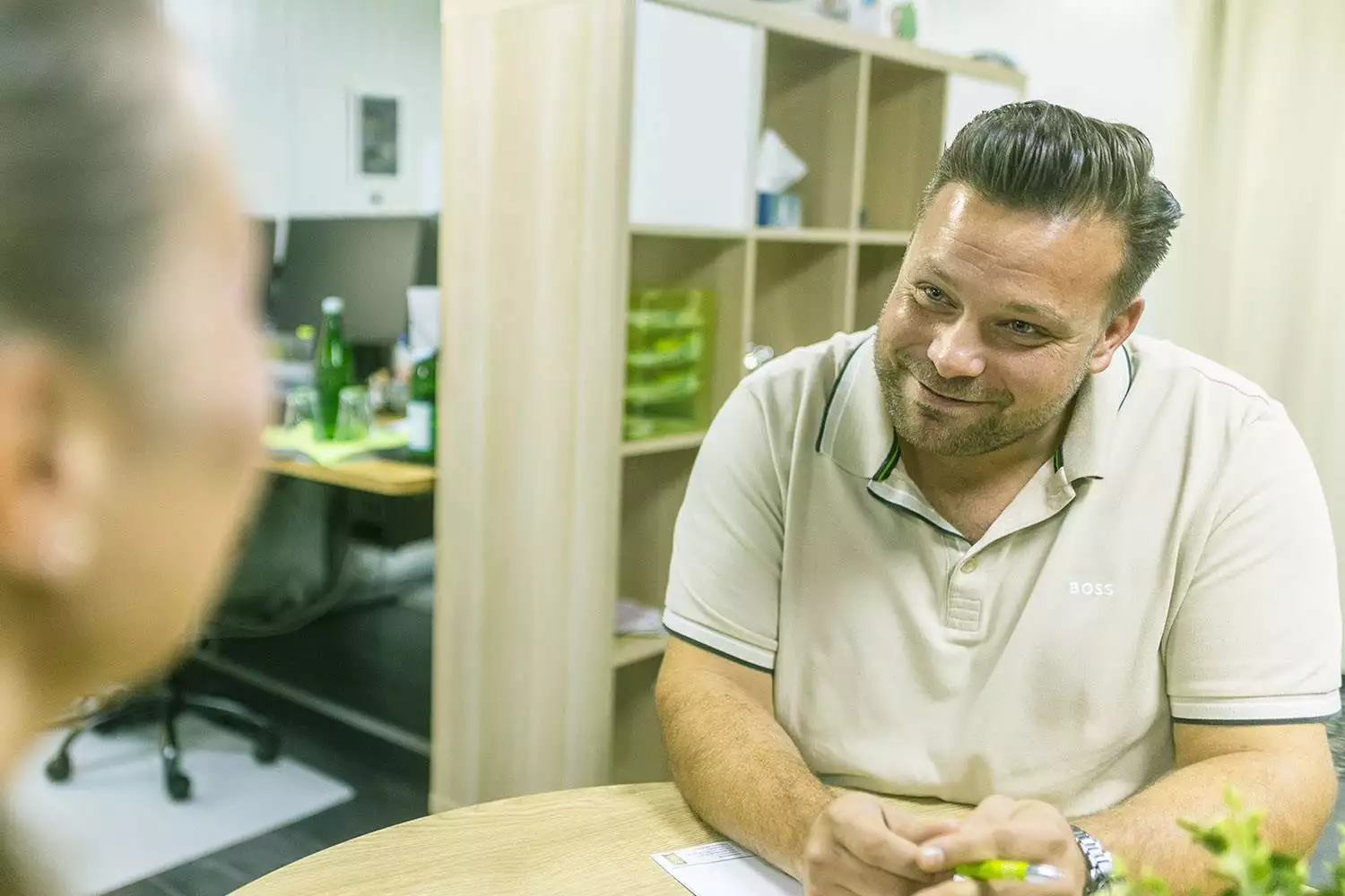 Ein Mann im Anzug hält ein Smartphone in der Hand, auf dem eine Liste von Kundenbewertungen mit Sterne-Bewertungen angezeigt wird. Im Hintergrund befinden sich eine Tastatur und ein Schreibtisch.