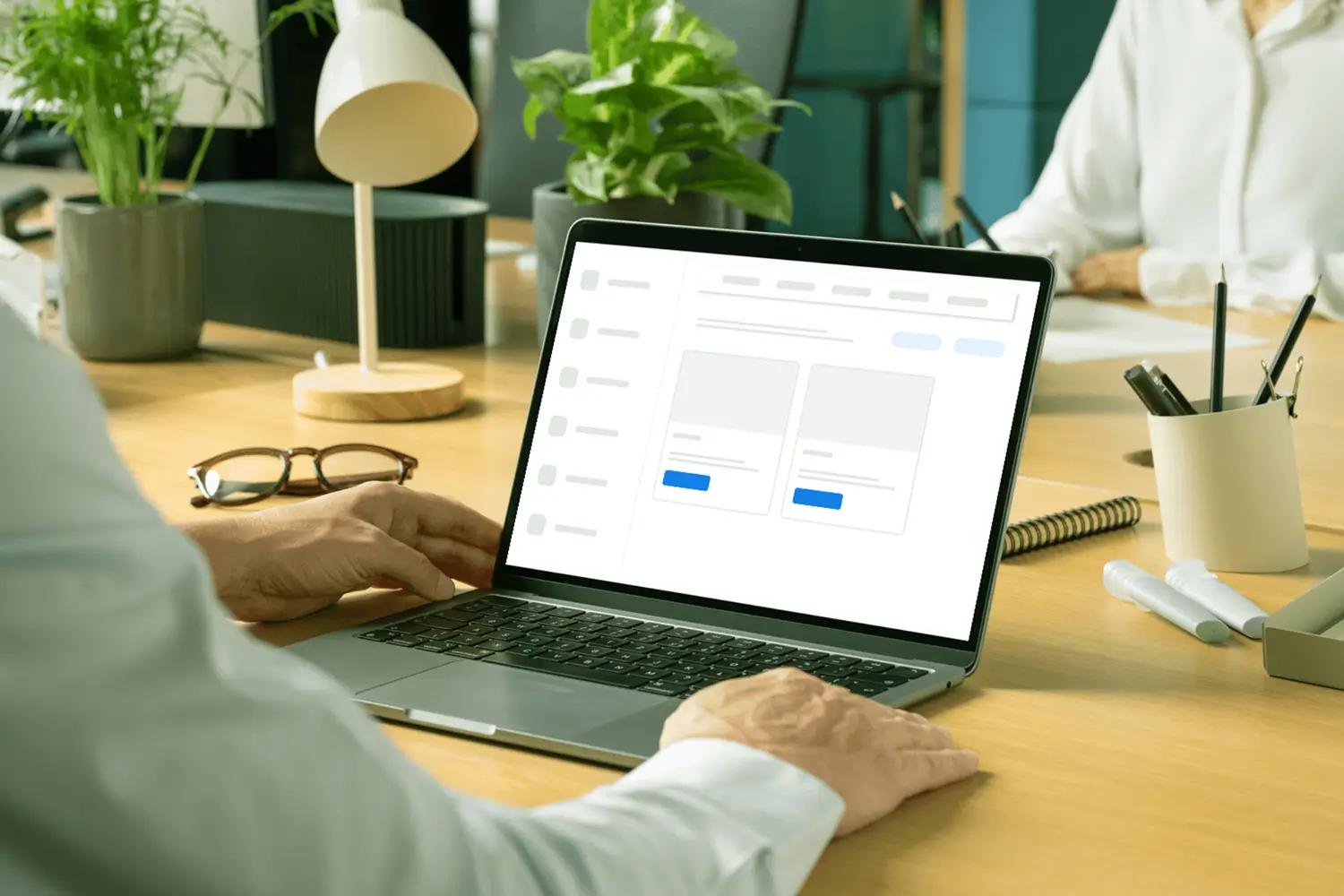 Person sitzt an einem Schreibtisch und betrachtet auf einem Laptop eine Seite mit Beitragsvorschlägen. Auf dem Schreibtisch liegen eine Brille, ein Notizblock, Stifte und Pflanzen, die für eine entspannte Arbeitsatmosphäre sorgen